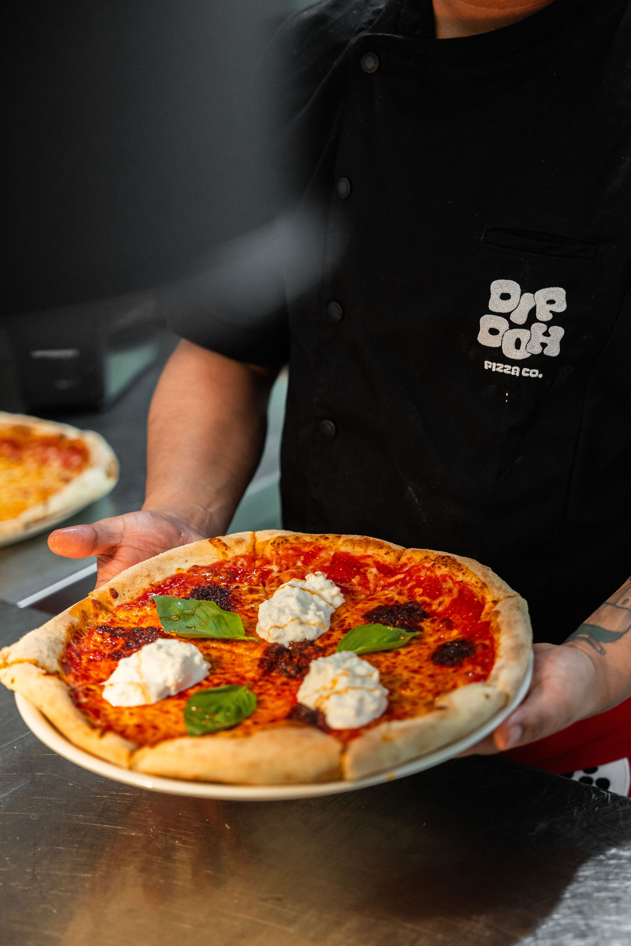 Dip Doh team member holding a freshly baked pizza topped with tomato, basil and cheese.